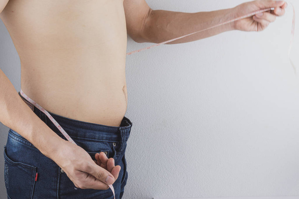 Close up shot of man with slim body measuring his waistline and  - 写真・画像