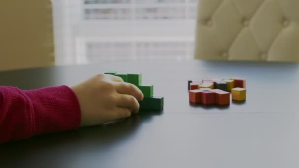small boy in a red sweater is playing with the colorful wooden blocks on a table in front of a window.Closeup video. - Imágenes, Vídeo