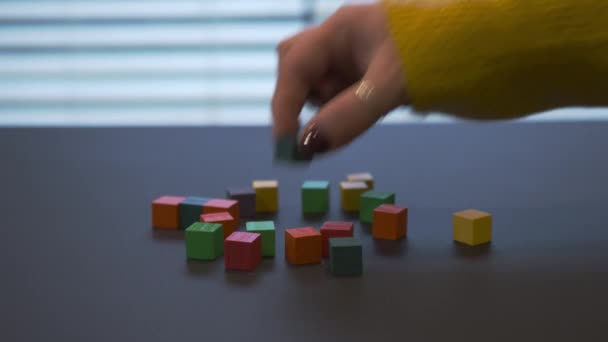 Young female hand with a red manicure in sweater mixing coloured wooden blocks and puting some of them in the middle. - Záběry, video