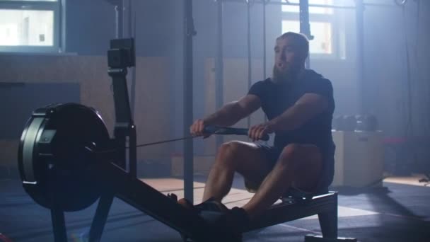 A strong man in slow motion pulls on a rope in a rowing simulator. Cardio training for one man in an atmospheric fitness room. - Footage, Video