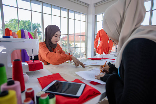 Kleines Geschäft muslimischer Modedesignerin, die im Bekleidungsgeschäft arbeitet und Smartphones und Tablets mit Kleidern benutzt - Foto, Bild