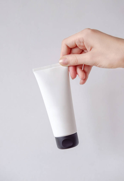 Joven mano femenina sostiene maqueta de embalaje cosmético minimalista. Mock-up para branding y etiqueta
. - Foto, Imagen