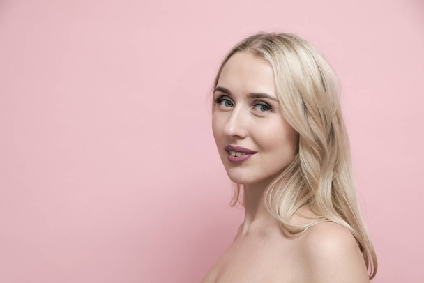 Beautiful blond woman with naked shoulders on pastel pink background. Beauty, cosmetics and skin care concept - Φωτογραφία, εικόνα