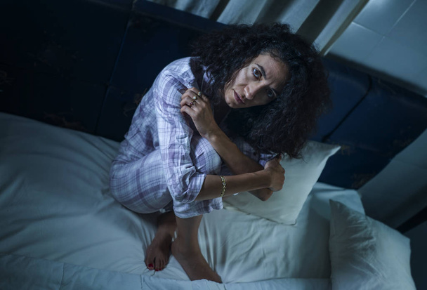 dramatic night lifestyle portrait of young sad and depressed latin woman with curly hair sleepless in bed awake and thoughtful feeling worried suffering depression - Foto, imagen