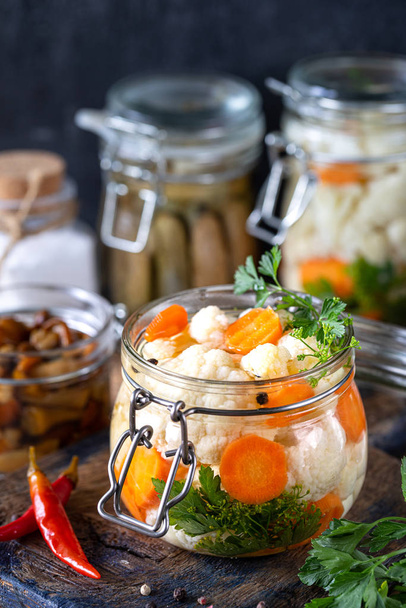 Pickled cauliflower with carrots in a glass jar on a dark wooden table. Fermented food. - Photo, Image