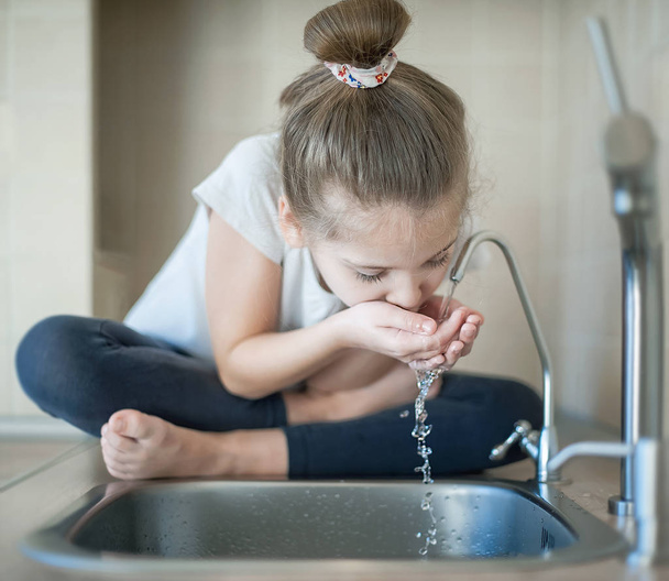 Caucasian cute girl is drinking from water tap or faucet - Foto, immagini