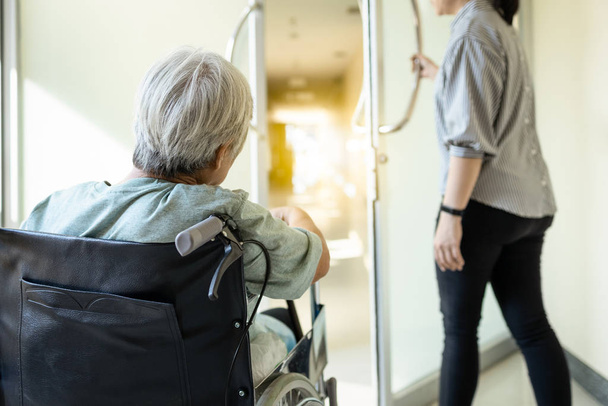 Stres asijské starší žena sedí na invalidním vozíku vykukuje ze dveří na chodbě nemocnice, starší pacient cítí strach, úzkost k léčbě nebo podstupuje operaci kolena, obává se zdravotních problémů - Fotografie, Obrázek