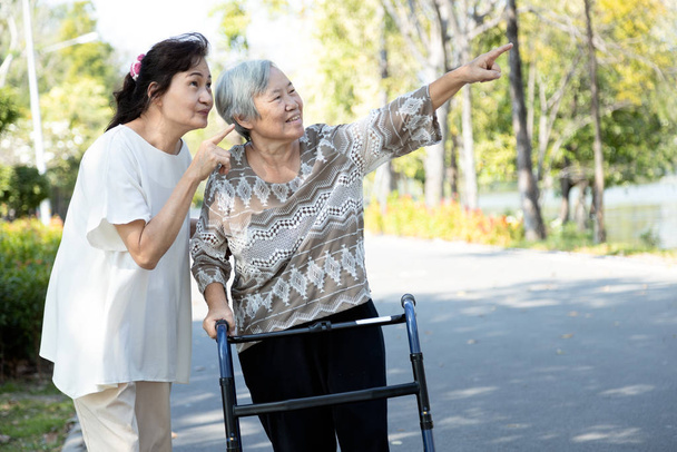 Feliz asiática senior mujer práctica caminar usando walker durante la rehabilitación, ancianos cuidado, apoyar a su mejor amigo, dos amigos divertirse disfrutando de un caminar juntos en un parque, friendshi
 - Foto, Imagen