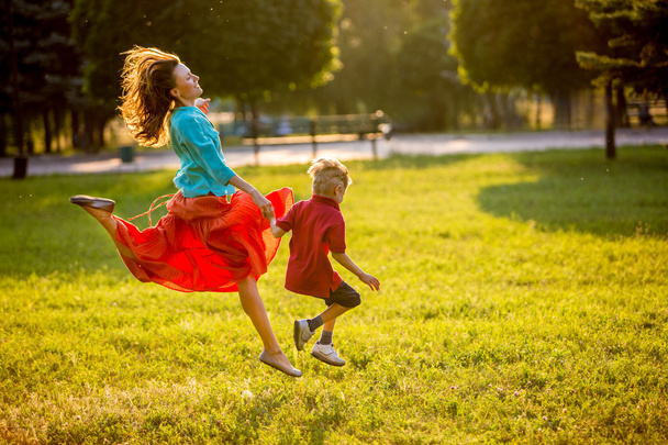 Carefree mother and child having fun in summer park, run and jump in motion. backlit - Φωτογραφία, εικόνα