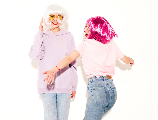 Two young sexy smiling hipster girls in wigs and red lips.Beautiful trendy women in summer clothes.Carefree models posing near white wall in studio.Positive female going crazy and dancing - Φωτογραφία, εικόνα