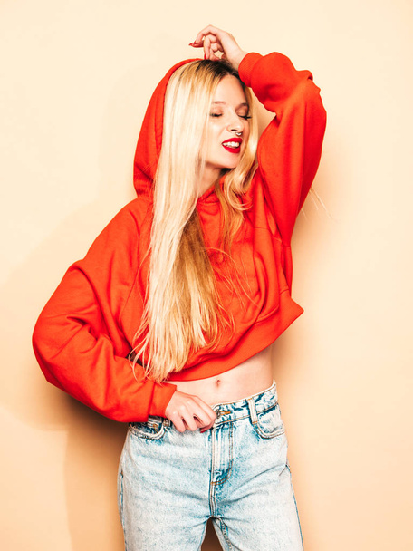 Portrait of young beautiful hipster bad girl in trendy red summer hoodie and earring in her nose.Sexy carefree smiling blond woman posing in studio.Positive model - 写真・画像