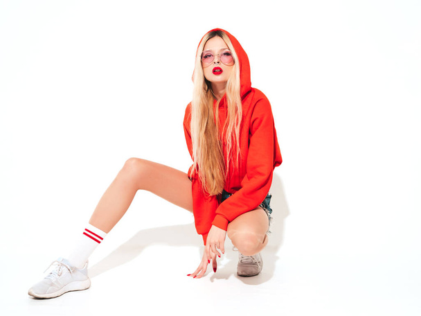 Portrait of young beautiful hipster bad girl in trendy red summer hoodie and earring in her nose.Sexy carefree smiling blond woman sitting in studio.Positive model having fun.Isolated on white - Fotoğraf, Görsel