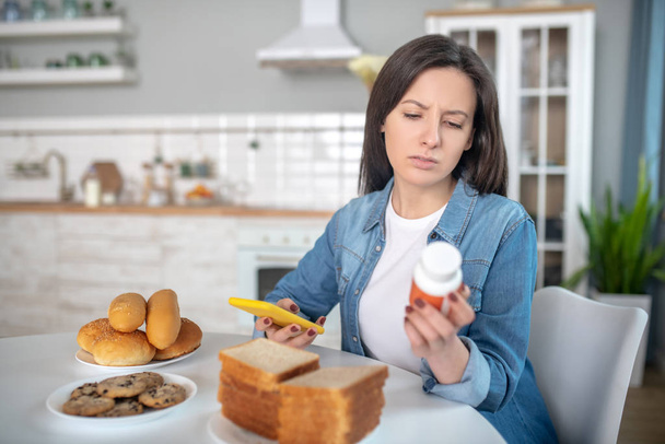 Woman looking at the pills while sitting in the kitchen - Foto, Bild