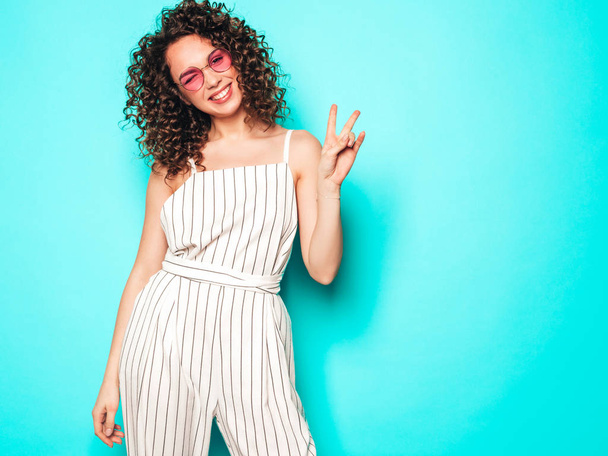 Portrait of beautiful smiling model with afro curls hairstyle dressed in summer hipster clothes.Sexy carefree girl posing near blue wall.Trendy funny and positive woman - Foto, afbeelding