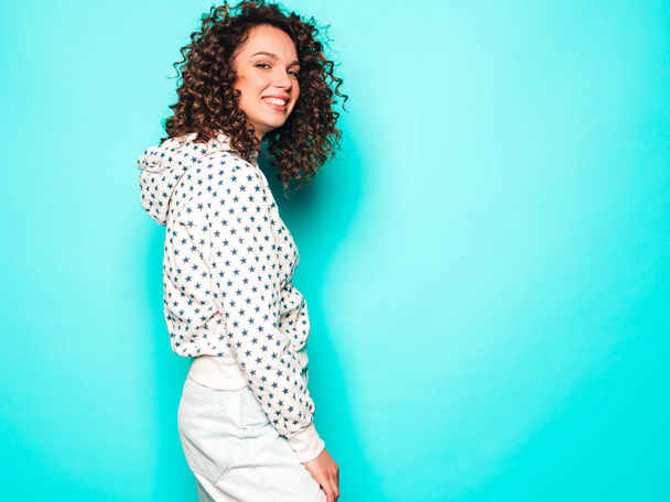 Portrait of beautiful smiling model with afro curls hairstyle dressed in summer hipster clothes.Sexy carefree girl posing near blue wall.Trendy funny and positive woman in white hoodie - Foto, Imagen