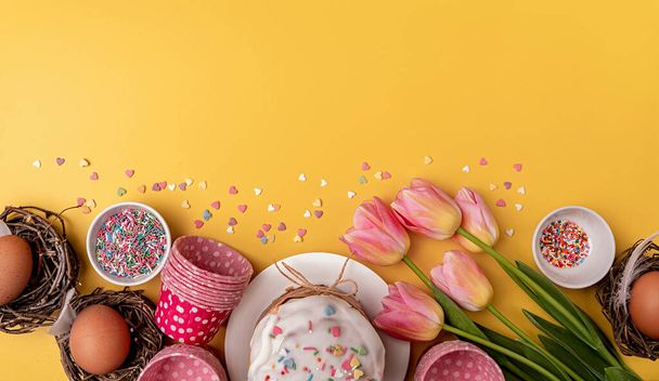 Paskalya pastası laleler, yumurtalar ve fırınlama öğeleri ile sarı arka planda fotokopi alanı ile üst görünüm - Fotoğraf, Görsel