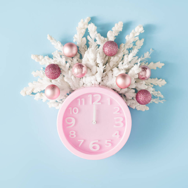 Creative winter layout made with pink clock and snowy branches with Christmas baubles. Minimal Christmas background flat lay. - 写真・画像