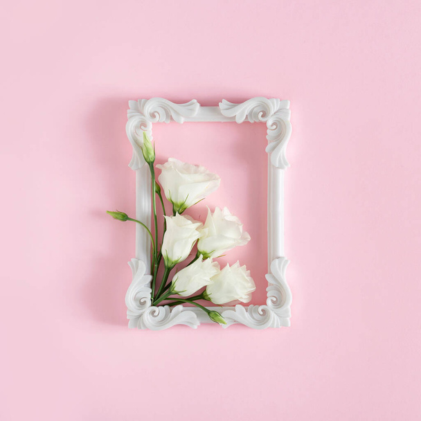 kreative Komposition aus weißen Rosenblüten und Rahmen auf rosa Hintergrund, Frauen Tag und Frühjahrssaison minimales Konzept  - Foto, Bild
