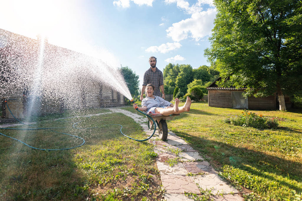 Young happy couple watering garden, a girl with a hose in hand o - Фото, зображення