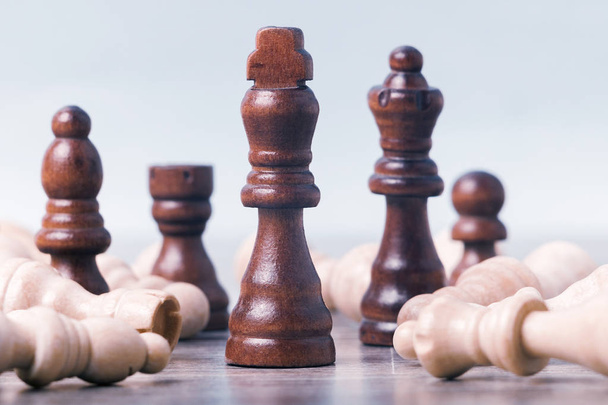 On the table are white chess pieces. The kings figure is in focus in the center; the remaining figures are out of focus. Around them are black pieces. The concept of business, success,  teamwork - Φωτογραφία, εικόνα