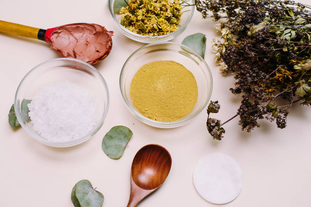 A bouquet of natural herbs and flowers next to bowls with natural clay, sea salt and dried chamomile. The concept of spa making homemade natural cosmetics - Photo, Image