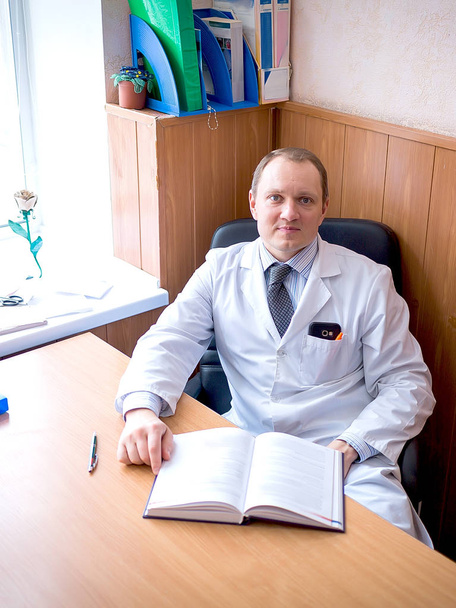 Arzt sitzt an seinem Arbeitsplatz am Tisch und lächelt - Foto, Bild