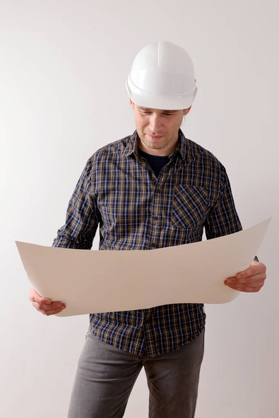 Young builder in a helmet, looks at a plan of the site. Isolated on a white background with text area. - Photo, Image