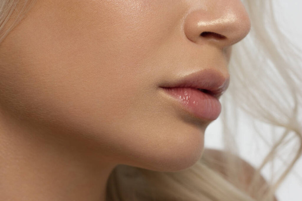 Close-up of woman's lips with fashion natural beige lipstick makeup. Macro sexy pale lipgloss make-up . Gentle pure skin and wavy blonde hair. Cosmetology, Spa, increase in lips - Fotoğraf, Görsel
