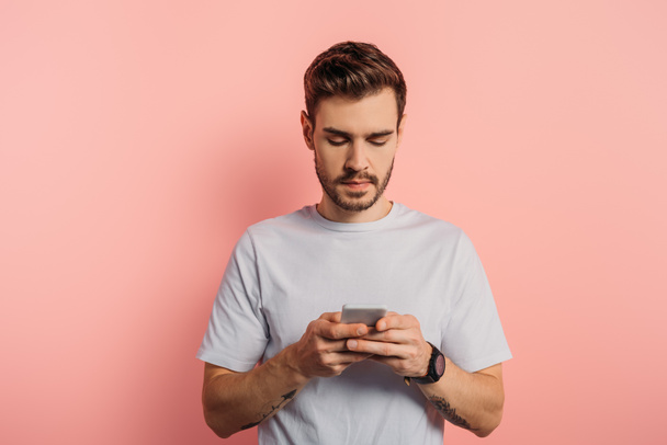 concentrated young man messaging on smartphone on pink background - Foto, afbeelding