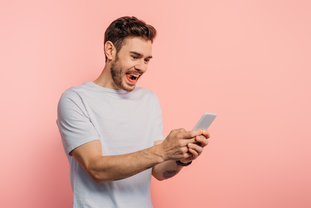 excited young man chatting on smartphone on pink background - Photo, Image
