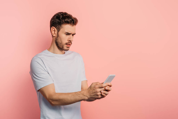 shocked young man chatting on smartphone on pink background - Photo, Image