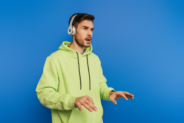inspired young man in wireless headphones imitating playing piano isolated on blue - Fotografie, Obrázek