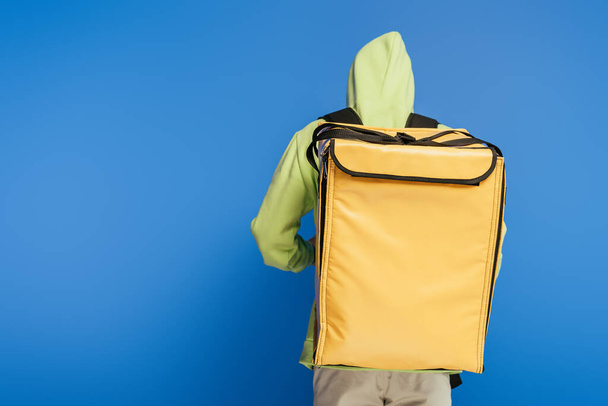 back view of delivery man carrying thermo backpack on blue background - Photo, Image