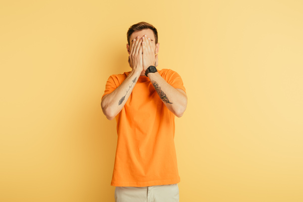 upset young man covering eyes with hands on yellow background - 写真・画像
