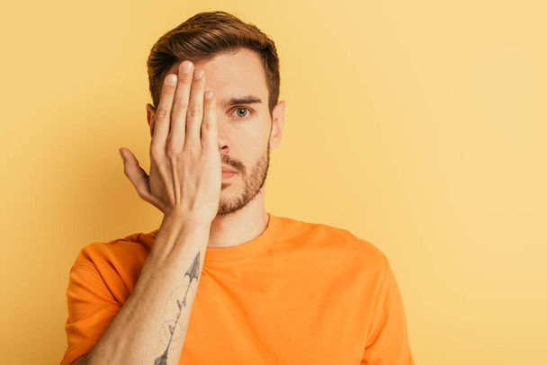 thoughtful handsome man covering eye with hand isolated on yellow - Photo, Image