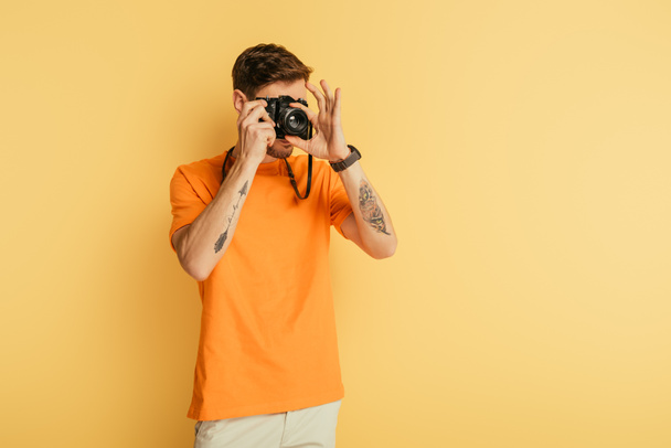 young tattooed photographer taking picture on yellow background - Foto, afbeelding