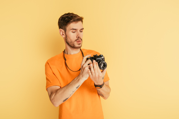 όμορφος προσεκτικός φωτογράφος κοιτάζοντας ψηφιακή φωτογραφική μηχανή σε κίτρινο φόντο - Φωτογραφία, εικόνα