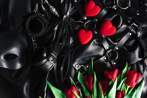 バレンタインデーには、黒い絹の背景に大人のおもちゃのセット。赤いチューリップ - 写真・画像