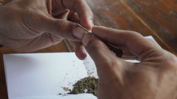 Close up man hands rolling marijuana joint and licking cigarette paper - 写真・画像