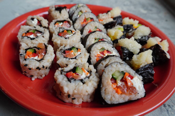 Sada domácích sushi nebo rohlíků s lososem, sezamová semínka podávaná na červeném talíři na šedém pozadí, vaření doma. - Fotografie, Obrázek