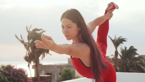 Close up young girl practice yoga standing bow pose on rooftop at sunset - Photo, Image