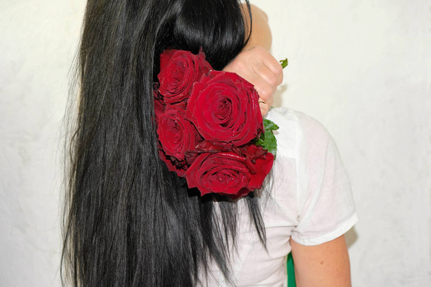 Mulher feliz com cabelos longos pretos em camisa branca voltou para trás. Ele tem um lindo buquê de rosas borgonhas no ombro. Mulher dentro de casa, em um fundo branco na Ucrânia
. - Foto, Imagem