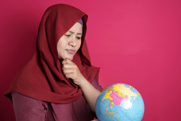 Felice donna musulmana indossa hijab rosso pensando mentre tiene in mano eart
 - Foto, immagini
