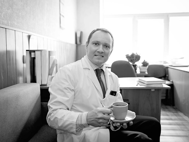 Beyaz önlüklü çekici doktor elinde bir fincan kahve tutuyor. - Fotoğraf, Görsel