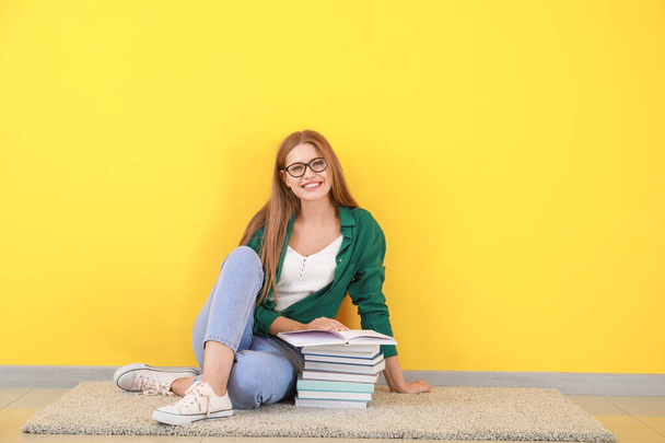Young woman with books sitting near color wall - Foto, Bild