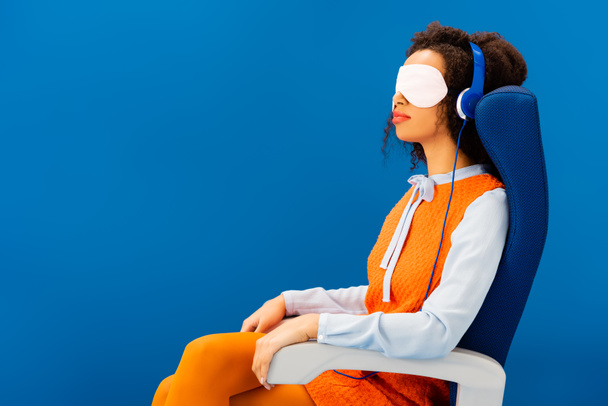 african american with sleeping mask listening to music and sleeping in seat isolated on blue  - Fotoğraf, Görsel