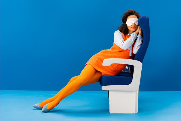 african american with sleeping mask sitting on seat and sleeping on blue background  - Fotó, kép