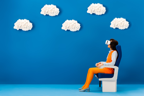 vue latérale du casque afro-américain en vr assis sur un siège sur fond bleu avec des nuages
  - Photo, image