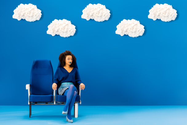 Afrykański Amerykanin siedzący na siedzeniu na niebieskim tle z chmurami  - Zdjęcie, obraz