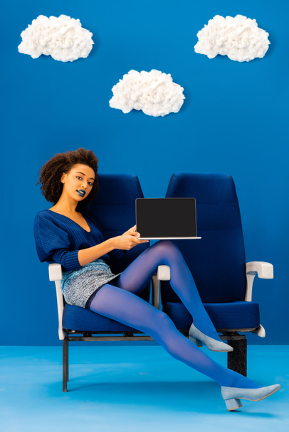 mosolygó afro-amerikai ül az ülésen, és tartsa laptop kék háttér felhők  - Fotó, kép